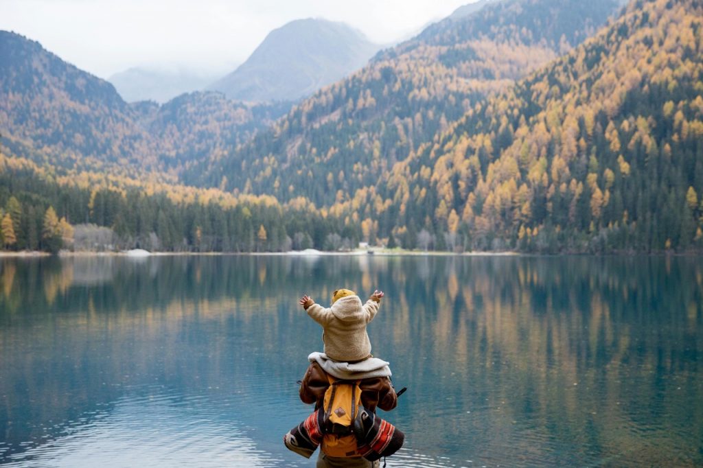 Image of a child on parents shoulders looking over a lake while travelling